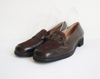 May include: A pair of brown leather loafers with suede accents on a white background. The shoes have a classic design with a decorative buckle and a low heel. The loafers are a size 8.