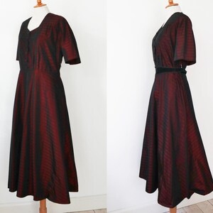 May include: A vintage-style dress with a V-neckline and short sleeves. The dress features a striking vertical striped pattern in black and burgundy. A black belt cinches the waist, enhancing the silhouette. The dress is displayed on a mannequin.