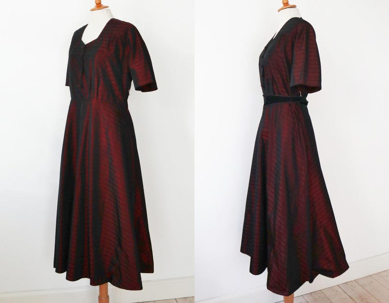 May include: A vintage-style dress with a V-neckline and short sleeves. The dress features a striking vertical striped pattern in black and burgundy. A black belt cinches the waist, enhancing the silhouette. The dress is displayed on a mannequin.