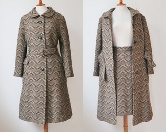 May include: A vintage two-piece suit featuring a long coat and skirt. The coat has a notched collar, button closure, and a matching belt. The fabric has a brown and beige chevron pattern. The skirt is knee-length and has a matching chevron pattern.