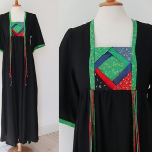 May include: A black maxi dress with short sleeves and a square neckline. The neckline and sleeve edges are trimmed with green fabric. The bodice features a colourful patchwork design, and red and green ribbons hang from the bodice.