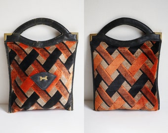 May include: Vintage handbag with a black leather handle and trim, featuring a geometric pattern in orange, black, and tan velvet. The bag has gold-toned corner accents and a diamond-shaped leather patch with a gold letter "H".