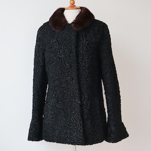 以下が含まれることがあります： 黒色のヴィンテージコート。テクスチャード加工のパターンと茶色の毛皮の襟が特徴です。ボタン留めのフロントと長袖が付いています。白い背景にマネキンで展示されています。