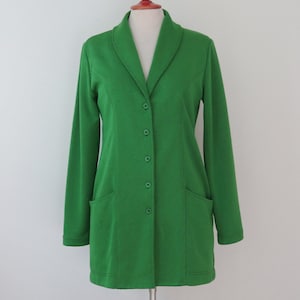 May include: A vibrant grass green blazer featuring a shawl collar, long sleeves, and a front button closure with five matching green buttons. The garment includes two patch pockets on the lower front and vertical seam detailing along the torso.