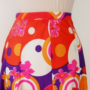 May include: A vibrant, high-waisted skirt featuring a bold, retro design. The skirt showcases a colorful pattern of large circles, flowers, and geometric shapes in shades of orange, white, purple, and pink. The fabric appears to be lightweight and flowing.