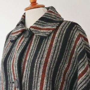 May include: A vintage coat with a striped pattern in black, white, and rust-red. The coat features a classic collar and two large black buttons. The fabric appears to be a textured wool blend, offering a warm and stylish outerwear option.