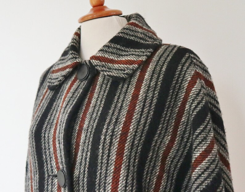May include: A vintage coat with a striped pattern in black, white, and rust-red. The coat features a classic collar and two large black buttons. The fabric appears to be a textured wool blend, offering a warm and stylish outerwear option.