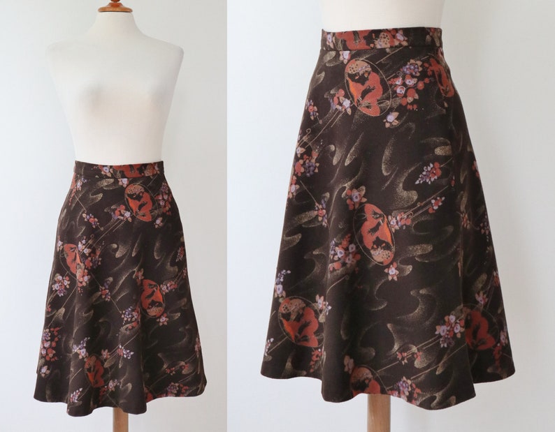 K&ouml;nnte beinhalten: A-Linien-Rock in dunkelbraunem Stoff mit floralem Muster. Der Rock hat eine hohe Taille und eine ausgestellte Silhouette. Das Muster umfasst orange, rosa und wei&szlig;e florale Elemente und abstrakte Formen.