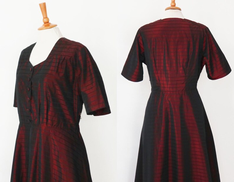 May include: A vintage, knee-length dress in a striking red and black color scheme. The dress features a V-neckline, short sleeves, and a button-down front. The fabric has a subtle sheen, with vertical black stripes over a red base, creating a textured appearance.