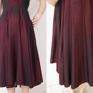 May include: A burgundy-colored dress with a flared skirt and a fitted bodice. The dress has a subtle sheen, and the fabric appears to have a slight ombre effect, transitioning from a darker shade at the top to a lighter hue towards the hem. The dress is knee-length.