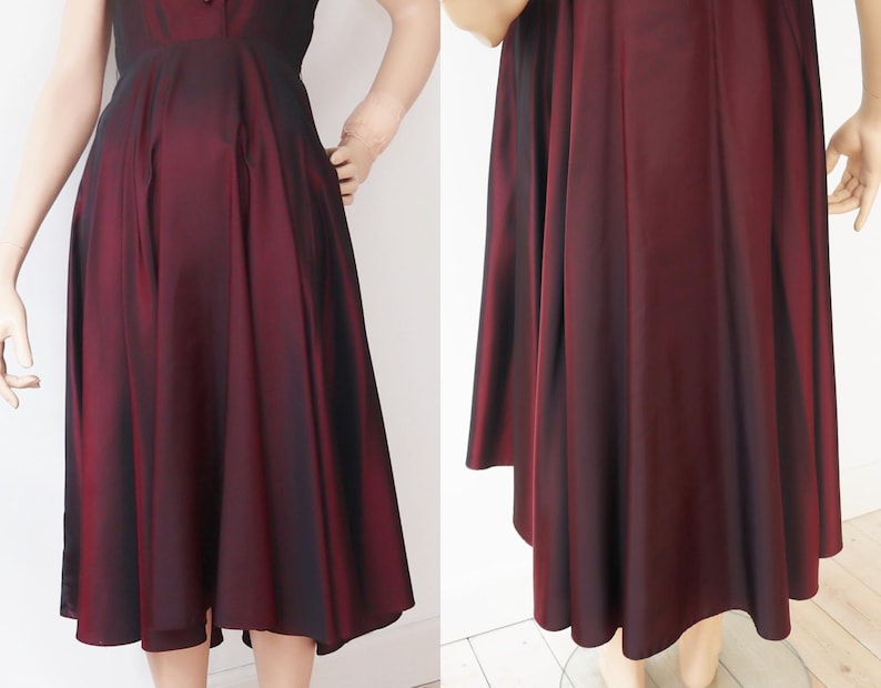 May include: A burgundy-colored dress with a flared skirt and a fitted bodice. The dress has a subtle sheen, and the fabric appears to have a slight ombre effect, transitioning from a darker shade at the top to a lighter hue towards the hem. The dress is knee-length.