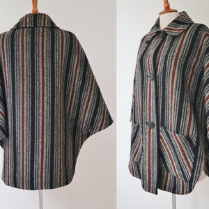 May include: A vintage cape with a striped pattern in black, gray, and rust-red. The cape features a collar, two large buttons, and two front pockets. The fabric appears to be a woven material, offering a classic, retro style.