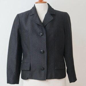May include: A dark grey blazer with a notched lapel, three-button fastening, and two front pockets. The jacket is displayed on a mannequin and has a classic, tailored design. A versatile piece of clothing.