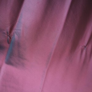 May include: Close-up of a fabric with a deep rose color. The fabric has a subtle sheen and is gathered in several places, creating small, stitched details. The folds and shadows add depth to the image.