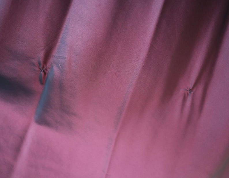 May include: Close-up of a fabric with a deep rose color. The fabric has a subtle sheen and is gathered in several places, creating small, stitched details. The folds and shadows add depth to the image.