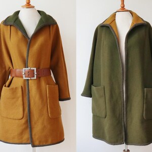 May include: Two long coats on mannequins. One is mustard yellow with a brown belt and large pockets. The other is olive green with large pockets. Both coats have contrasting trim and collars.