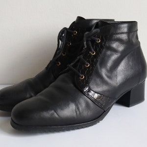 Puede incluir: Botines de cuero negro con cordones. Los botines presentan un panel texturizado en los laterales y un pequeño tacón cuadrado. Fondo blanco.