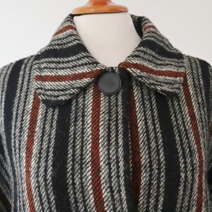 May include: A close-up of a vintage coat with a striped pattern in black, white, and rust-colored stripes. The coat features a large collar and a single black button closure. The fabric appears to be a woven wool or wool blend.