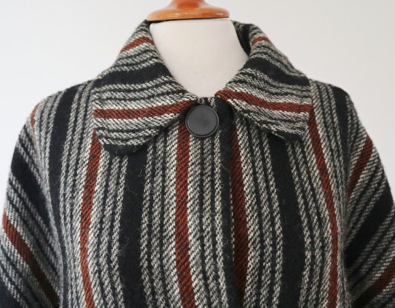 May include: A close-up of a vintage coat with a striped pattern in black, white, and rust-colored stripes. The coat features a large collar and a single black button closure. The fabric appears to be a woven wool or wool blend.