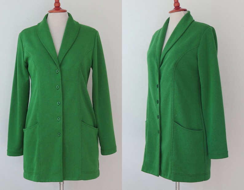 May include: A vibrant green blazer featuring a shawl collar, long sleeves, and a front button closure with four matching green buttons. The garment includes two front patch pockets and is displayed on a mannequin to show the front and side profile.