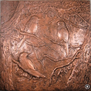 Op de afbeelding: Een koperen reliëfsculptuur van drie vogels die op takken zitten. De vogels bevinden zich in een natuurlijke omgeving met bladeren en takken. De sculptuur is gedetailleerd en realistisch.