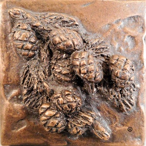 May include: A close-up of a bronze sculpture of a cluster of pine cones. The sculpture is textured and detailed, with each pine cone individually sculpted.