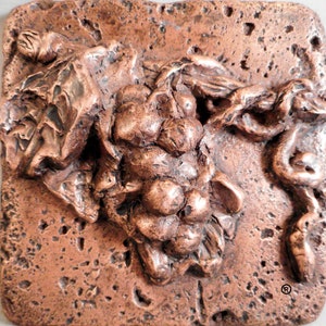 May include: A copper-colored wall plaque with a raised design of a bunch of grapes. The grapes are clustered together and have a textured surface. The plaque has a rough, textured surface.