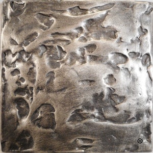 May include: A close-up of a textured, silver metal tile with a hammered finish. The tile has a rough, uneven surface with a metallic sheen.