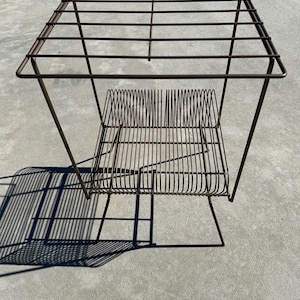 May include: A metal wire shelf unit with two tiers. The top tier is a square shape and the bottom tier is a rectangular shape. The shelf unit is made of thin metal wire and has a dark brown finish.
