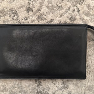 Könnte beinhalten: Eine schwarze Leder-Clutch mit Reißverschluss.