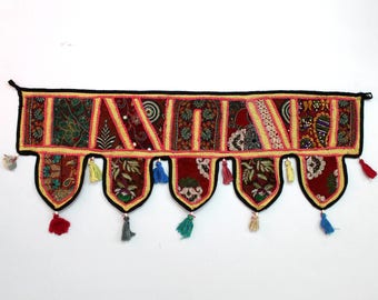 May include: A decorative textile banner with a red background and intricate embroidery. The banner features a black border, yellow accents, and colorful tassels. The design includes floral patterns and the word "INDIA" in a stylized font.