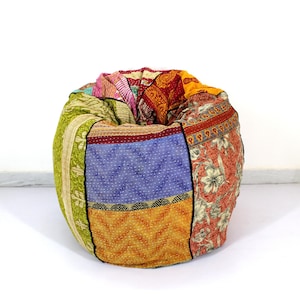 May include: A round beanbag chair made from patchwork fabric. The beanbag features a variety of colors and patterns, including floral, geometric, and striped designs. The chair is a mix of red, blue, green, and yellow fabrics. The beanbag is a comfortable seating option.