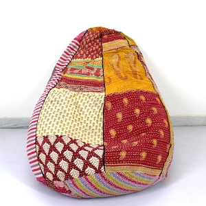 May include: A large, colorful bean bag chair made from patchwork fabric. The fabric is a mix of red, yellow, pink, and white with various patterns. The chair is filled with beans and is perfect for lounging.