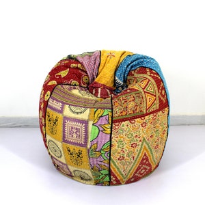 Puede incluir: Un puf redondo con un diseño de patchwork. El puf presenta una variedad de telas coloridas, incluyendo rojo, amarillo, azul y morado. Las telas tienen patrones florales y geométricos. El puf está sobre un fondo blanco.