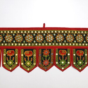 Op de afbeelding: Een rode en zwarte stoffen deurhanger met geborduurde olifanten, bloemen en spiegelaccenten.