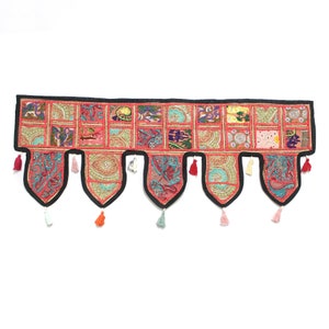 May include: A colorful patchwork fabric door hanging with tassels. The hanging is made of red, pink, blue, green, and yellow fabric. The tassels are made of white, pink, and orange thread.