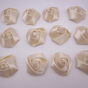 May include: Twelve ivory satin fabric rose flower embellishments. Each flower is approximately 2 inches in diameter.
