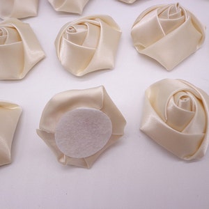May include: Ten ivory satin fabric rose flower embellishments with a felt backing. The roses are approximately 2 inches in diameter.