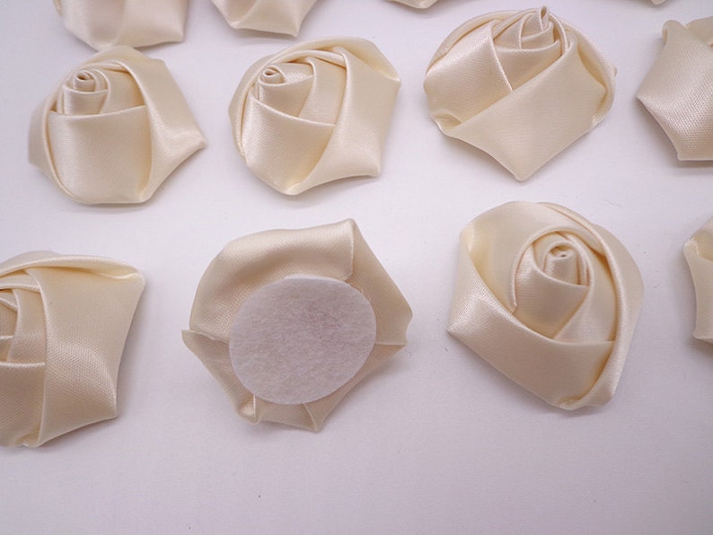 May include: Ten ivory satin fabric rose flower embellishments with a felt backing. The roses are approximately 2 inches in diameter.