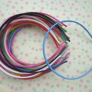 May include: A collection of colourful plastic headbands, including black, white, pink, blue, green, and yellow. The headbands are arranged in a circle, with one blue headband lying outside the circle.