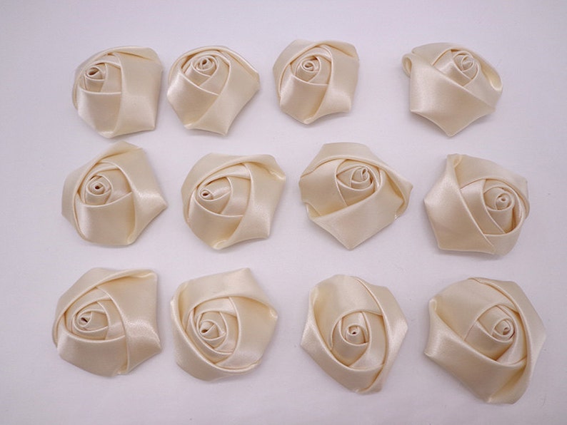 May include: Twelve ivory satin fabric rose flower embellishments. Each rose is approximately 2 inches in diameter.
