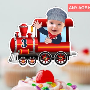 Op de afbeelding: Een rode en zwarte speelgoedtrein caketopper met een babygezicht in het raam. De trein heeft het nummer 3 aan de zijkant.  ANY AGE NUMBER staat rechtsboven.