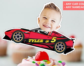 May include: A red race car cake topper with a child's face, the name "TYLER" and the number "5" on the side. The text "- ANY CAR COLOR - ANY NAME/AGE" is in the top right corner. The topper is placed on top of a cupcake.