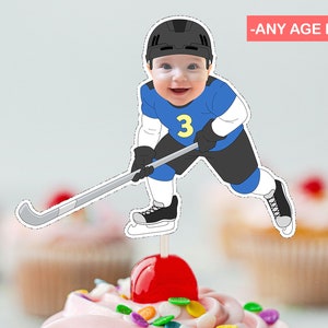 Może przedstawiać: Topper na tort w postaci hokeisty w niebieskim i czarnym stroju z kijem i numerem 3 na koszulce. Hokeista ma uśmiechniętą twarz i nosi kask. Topper znajduje się na muffince z różowym lukrem i posypką.