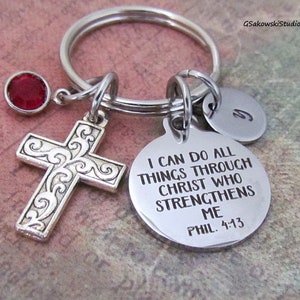May include: Silver-toned keychain with a cross pendant, a red gemstone, and a circular charm engraved with the text "I CAN DO ALL THINGS THROUGH CHRIST WHO STRENGTHENS ME PHIL. 4:13". Includes a small, round charm with the letter "G".