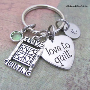 May include: Silver keychain with a heart charm that says "love to quilt", a charm with a quilt block design that says "I love quilting", and a small green gemstone charm.