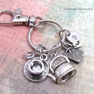 May include: Silver-toned keychain with charms. Charms include a teacup and saucer, a teapot, a heart, and a charm that says "TEA". The keychain has a lobster claw clasp.