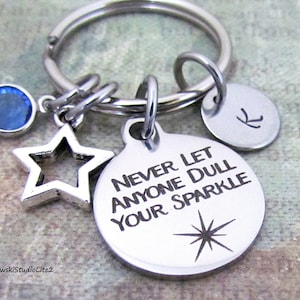May include: A silver keychain with a blue rhinestone, a star charm, and a round charm with the text "Never let anyone dull your sparkle" and a star design.