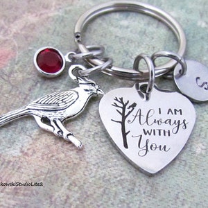 May include: A silver heart-shaped keychain with the text "I am Always With You" and a small cardinal charm. The keychain also has a small red rhinestone charm and a silver charm with the letter "S".