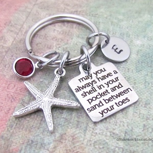 May include: Silver keychain with a red gem, a starfish charm, and a square tag with the text "may you always have a shell in your pocket and sand between your toes".